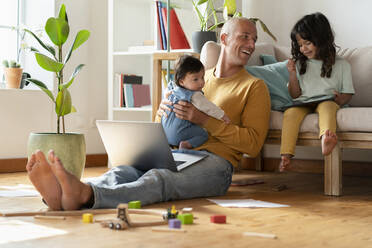 Lächelnder Vater mit Laptop, der mit seinen Töchtern zu Hause spielt - SBOF03373