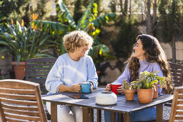 Smiling mother and daughter having coffee while sitting at front yard - MPPF01572