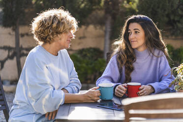 Reife Frau im Gespräch mit junger Frau, während sie im Hinterhof sitzt - MPPF01577