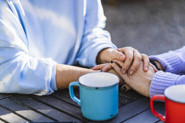 Mother and daughter with hands stacked on table at back yard - MPPF01578