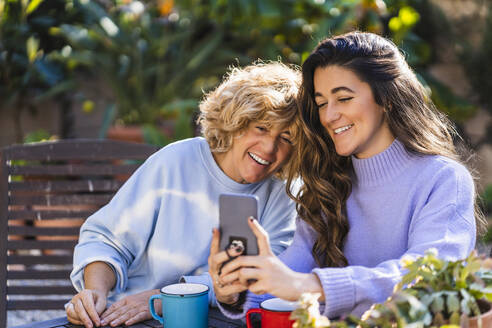 Smiling young woman taking selfie with mature female through mobile phone at back yard - MPPF01579