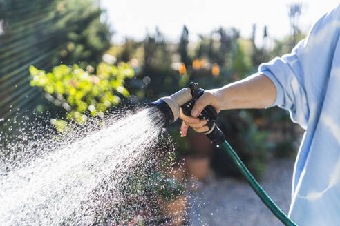 Frau bewässert mit Gartenschlauch im Vorgarten - MPPF01590