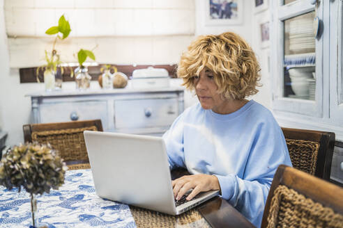 Reife Frau arbeitet am Laptop, während sie zu Hause sitzt - MPPF01600