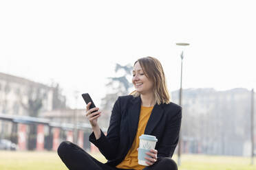 Smiling entrepreneur with disposable cup using mobile phone - EIF00663