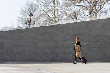 Businesswoman walking with suitcase and jacket on footpath - EIF00687