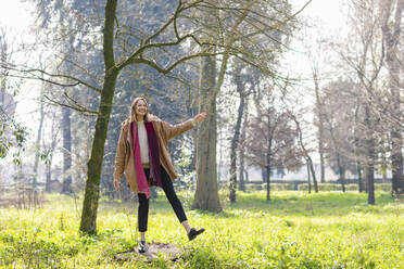 Playful woman standing on tree stump at park - EIF00695