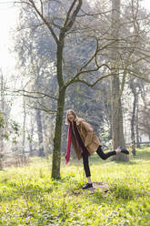 Carefree woman standing on tree stump at park - EIF00696