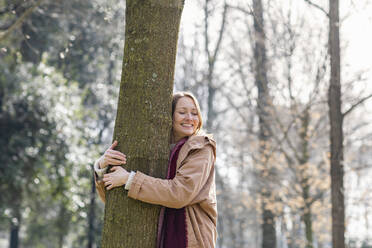 Smiling woman embracing tree at park - EIF00699