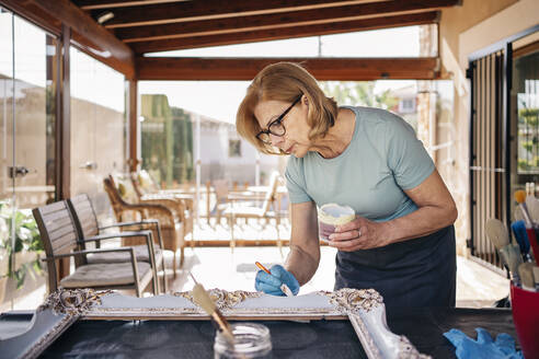 Blonde ältere Frau malt Rahmen im Sonnenzimmer - AMPF00125