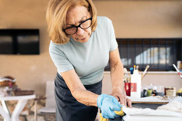 Senior woman wiping frame with rag at home - AMPF00126