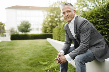 Male restaurateur sitting on retaining wall by plants - SAJF00123