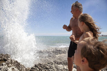 Father with children looking at water splash while standing on rock - AUF00575