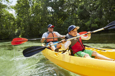 Boy with father in life jacket canoeing with oar in lake during picnic - AUF00578