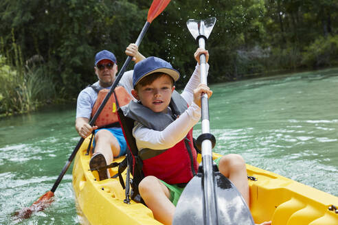 Cute boy and father canoeing in lake during vacation - AUF00580