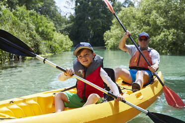 Smiling boy looking away while canoeing with father in lake - AUF00581