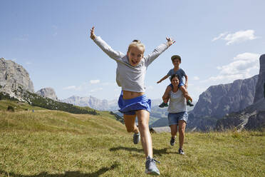 Carefree girl with arms raised running with mother carrying son against sky - AUF00587