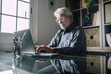 Seriöser älterer männlicher Unternehmer mit Brille, der einen Laptop im Heimbüro benutzt - SIPF02302