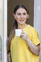 Smiling woman looking away while having coffee at window - OGF00964