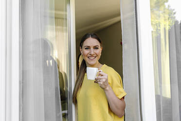 Schöne lächelnde Frau beim Kaffee trinken am Fenster stehend - OGF00970