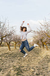 Carefree young woman jumping at almond trees - MGRF00185