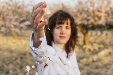 Young woman playing with almond blossom petal - MGRF00196