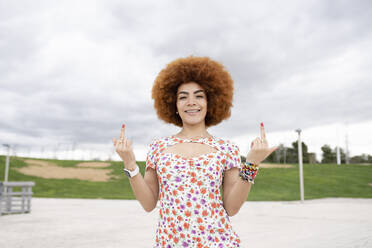 Lächelnde Frau gestikuliert obszönes Handzeichen im Park - JCCMF01472