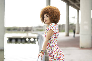 Redhead woman in floral dress standing by railing at park - JCCMF01483