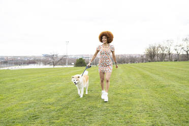 Smiling woman holding leash while walking with dog at park - JCCMF01503