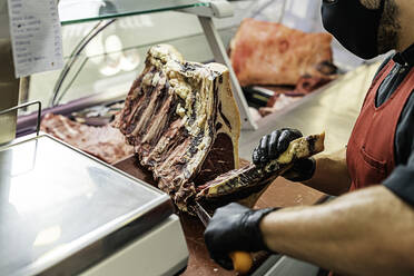 Professioneller Fleischer mit Maske, der Fleisch zubereitet und zerlegt - CAVF93731