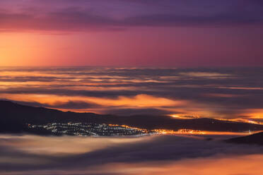 Aerial view of modern city and mountains covered with tick clouds under colorful sky during sunrise - ADSF22053