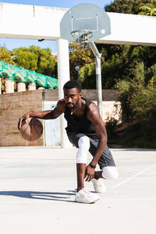 Entschlossener afroamerikanischer männlicher Sportler, der im Sommer auf dem Platz Basketball spielt und in die Kamera schaut - ADSF22089