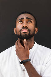 Confident African American male wearing white t shirt standing on street while looking up - ADSF22094