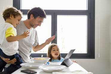 Vater und Sohn winken mit der Hand während eines Videoanrufs über ein digitales Tablet durch ein Mädchen zu Hause - IFRF00460
