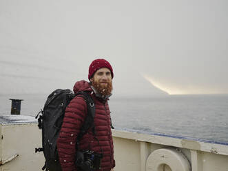 Bärtiger Mann schaut in die Kamera, während er sich auf einer Fähre auf den Färöer Inseln befindet - CAVF93747