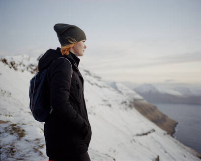 Frau steht auf einem verschneiten Berggipfel und blickt auf das Meer - CAVF93754