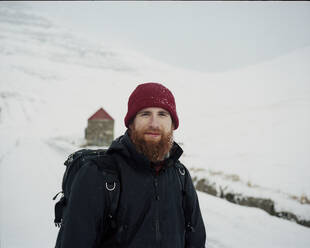 Porträt eines lächelnden, bärtigen Mannes im Schnee, der in die Kamera schaut, auf den Färöer Inseln - CAVF93756