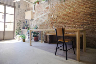 Stuhl und leerer Tisch stehen drinnen vor einer Backsteinmauer - VABF04284