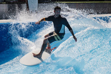 Sportler mit Surfbrett beim Surfen auf einer Schwimmbadwelle - MRRF00948