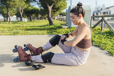 Woman with protective sportswear and roller skates sitting on concrete - JRVF00382