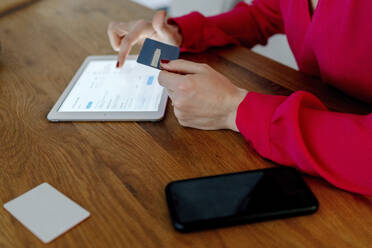 Woman making card payment while buying on internet using digital tablet at table - OGF00984