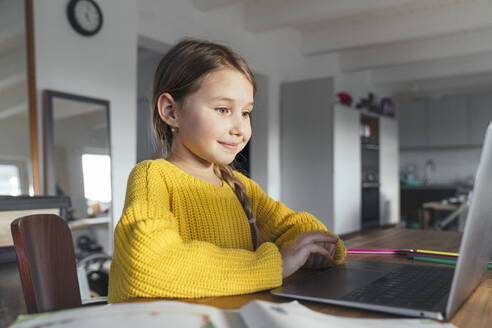 Smiling cute girl using laptop on table at home - KMKF01633