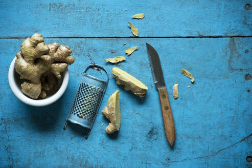 Ingwerwurzel, Reibe und Küchenmesser liegen auf einer blauen Holzfläche - ASF06741