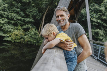 Smiling man carrying son leaning over railing - MFF07643