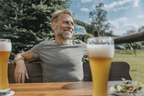 Lächelnder reifer Mann, der wegschaut, während er im Biergarten sitzt - MFF07644