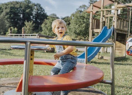 Charmanter Junge sitzt auf einem Karussell auf dem Spielplatz - MFF07650