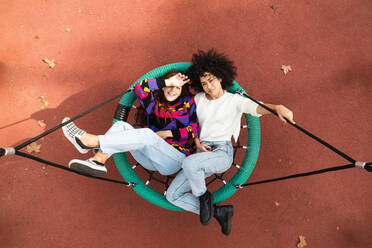 Top view of friendly multiracial female best friends lying on net swing on playground while relaxing and looking at camera - ADSF22175