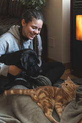 Smiling female teenager sitting with pets at home - JAQF00400