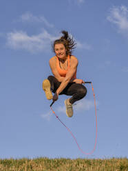Young woman jumping rope in front of blue sky - STSF02882