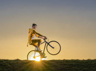 Junger Mann macht Fahrradstunts bei Sonnenuntergang - STSF02884