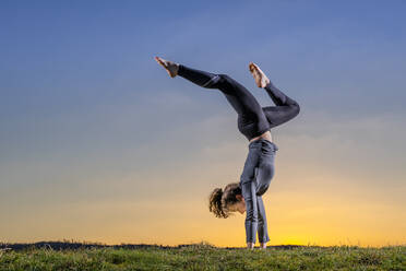 Flexible Frau macht Handstand auf Gras bei Sonnenuntergang - STSF02889